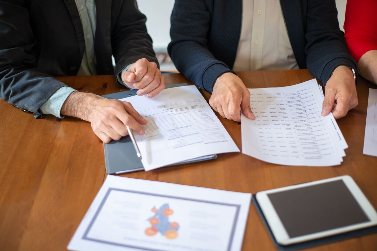 Two senior executives reviewing documents at a boardroom table while comparing proposals