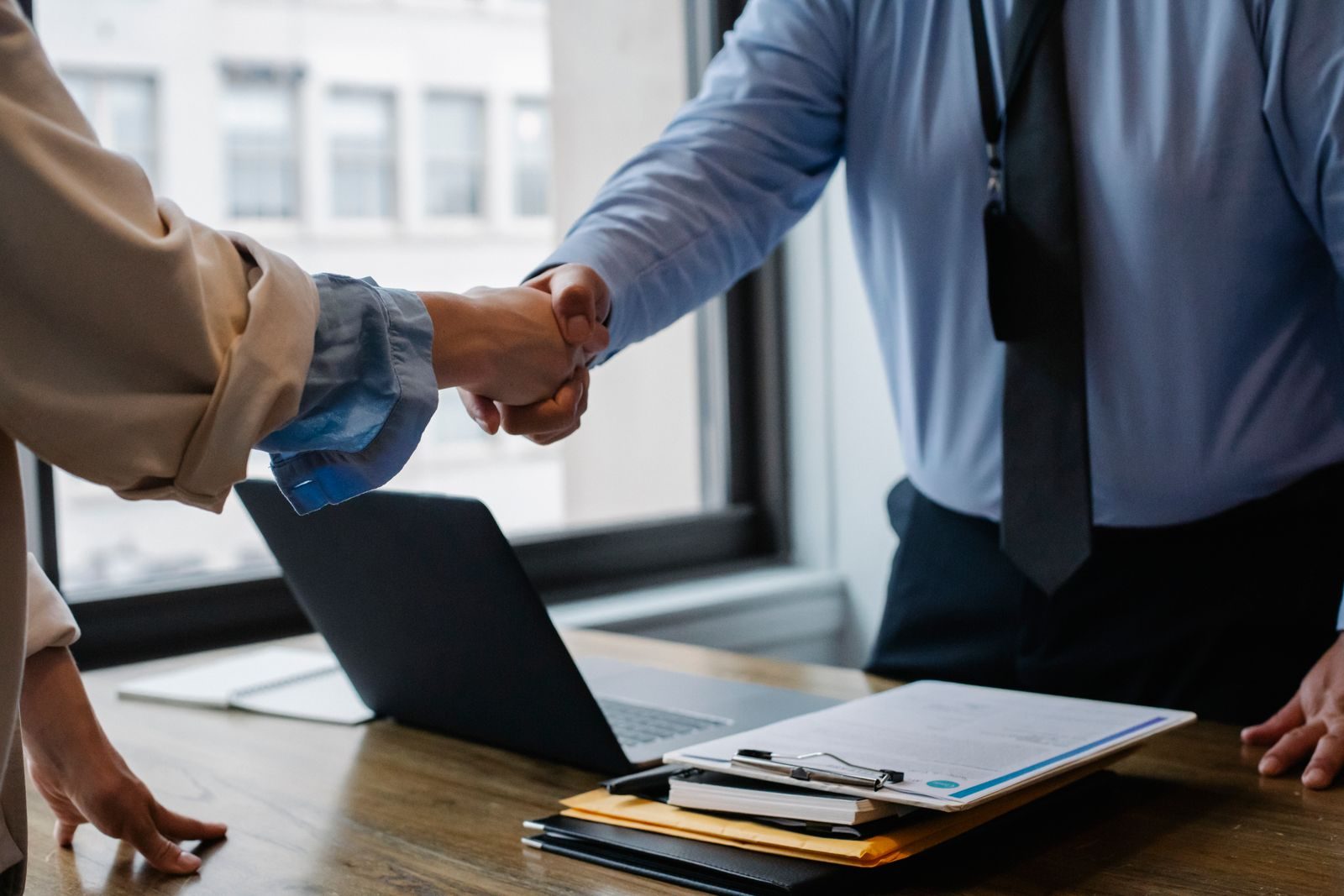 Two executives shaking hands over a signed coaching agreement on a boardroom table