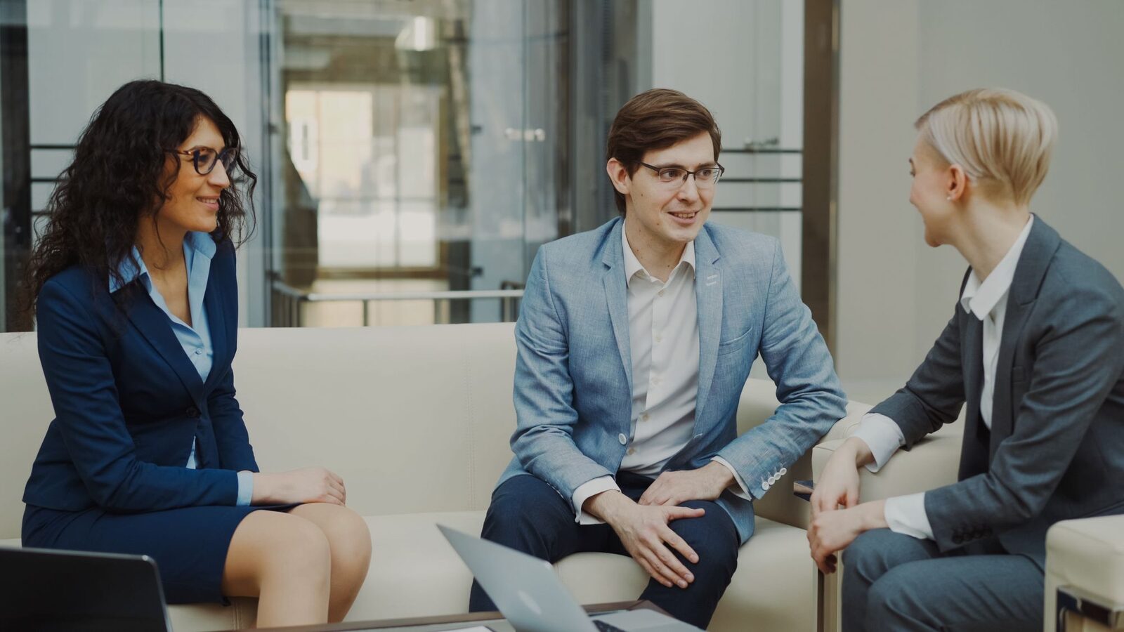 Three professionals in a candid peer conversation in a bright office lobby
