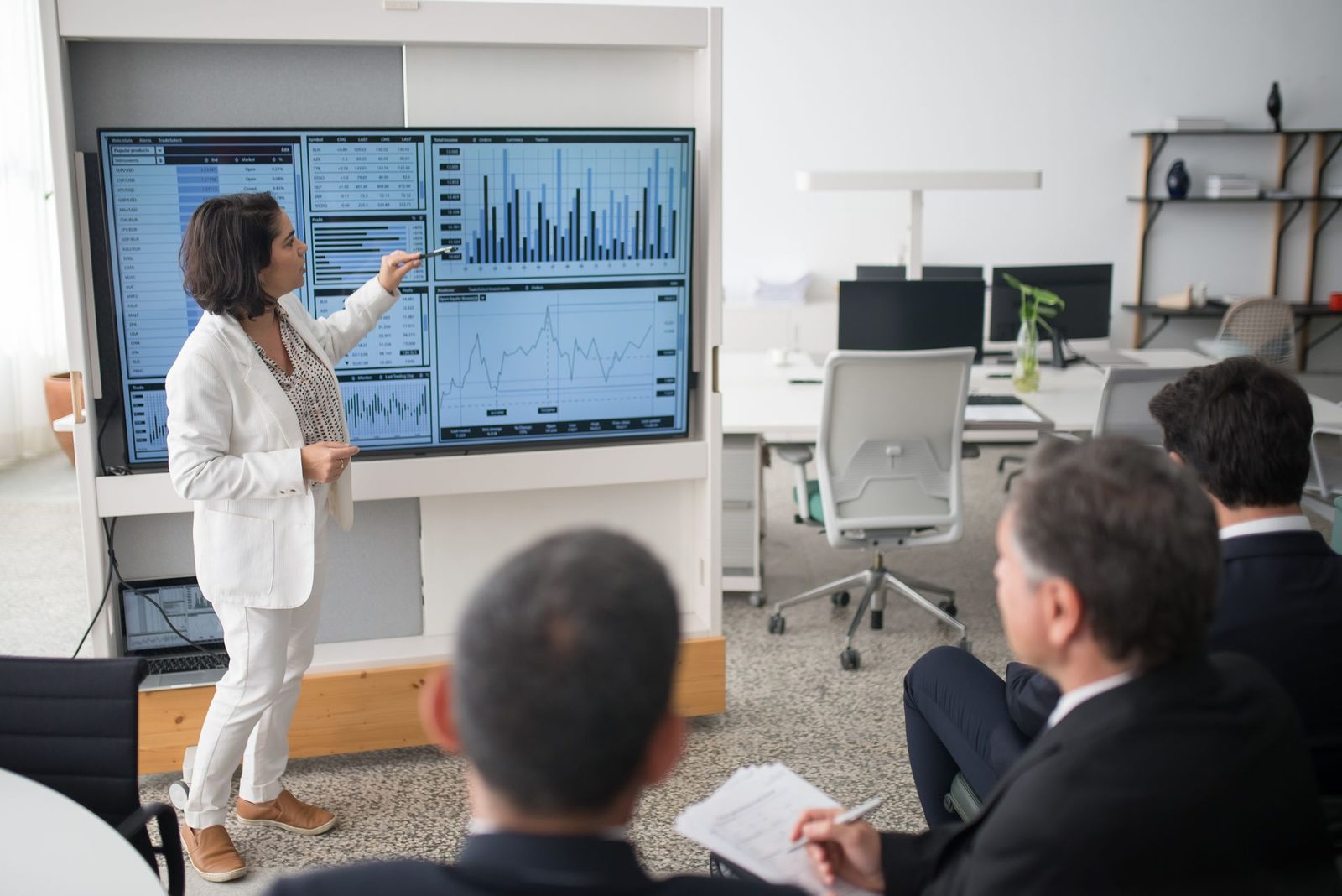 A senior leader presenting to executives around a boardroom screen